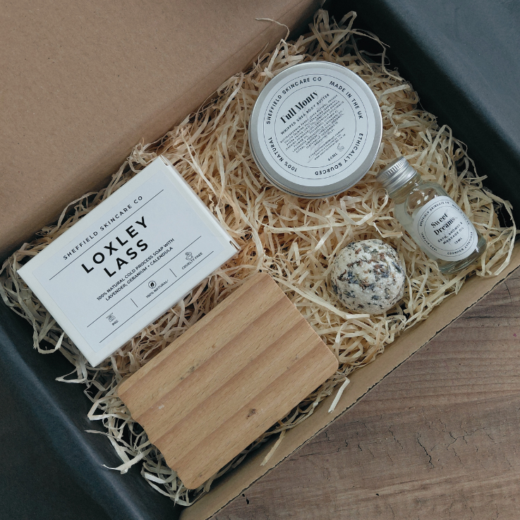 Set of beauty products including a bar of soap, cream, and other items in a box with natural materials.